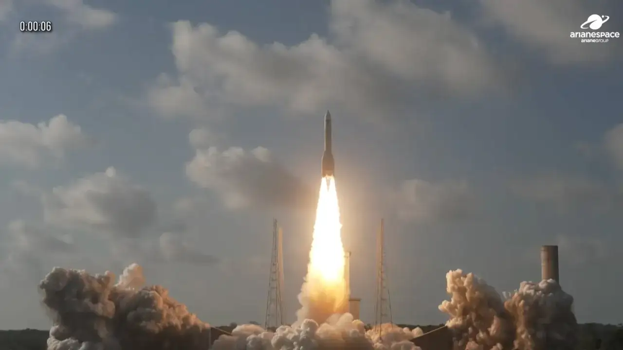 Ariane 5 rocket launching with bright flames and smoke against a cloudy sky.