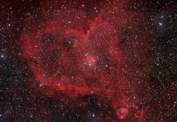 Ett kosmiskt hjärta av rött gasmoln och stjärnor, en hjärtnebulosa som lyser i rymden.