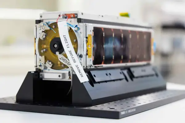 En satellit från Saab Aerospace, redo för rymden. En vit etikett med texten "REMOVE BEFORE FLIGHT" är fäst vid enheten.