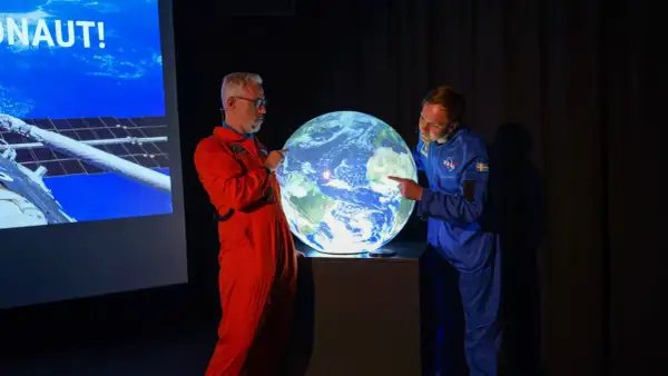 Två män i rymddräkter pekar på en lysande jordglob, som representerar vår planet.