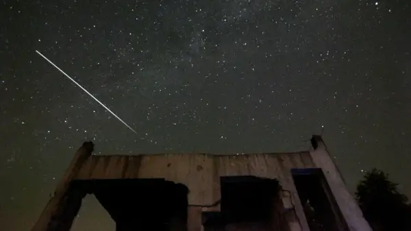 En ljus meteor drar en strimma över en stjärnklar natthimmel, ovanför ruinerna av en byggnad.