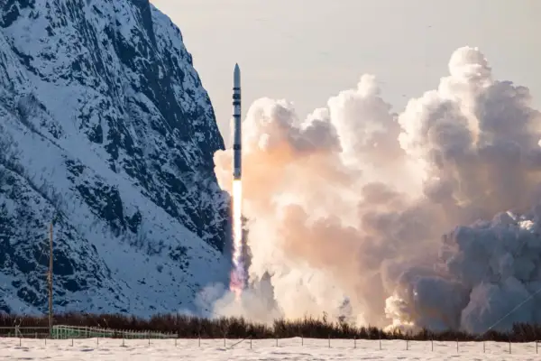 ISAR Aerospace raket skjuter upp från en snötäckt mark, med en snöig bergssida och moln i bakgrunden.