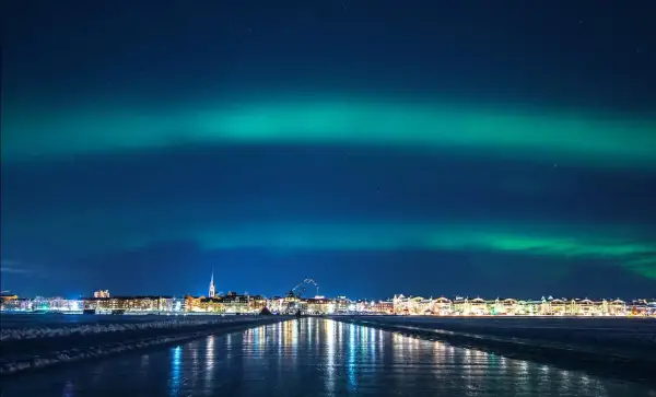 Luleå norrsken lyser upp himlen över en stad vid en isig kustlinje.