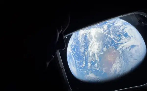 Silhuett av en person som tittar ut genom ett fönster på jorden från rymden. ISS Sverige.
