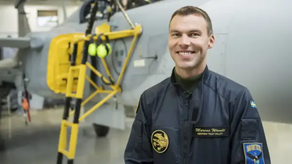 Marcus Wandt, Gripen testpilot, ler glatt framför ett stridsflygplan.
