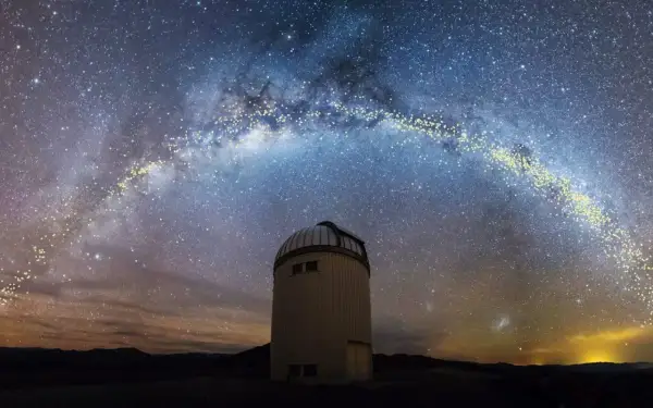 En kupolformad observatoriebyggnad står under en magnifik vintergatan från jorden. Stjärnorna lyser starkt mot den mörka himlen.