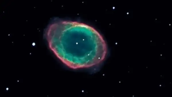 Den kosmiska ringnebulosan lyser i grönt och rosa mot en mörk stjärnhimmel.